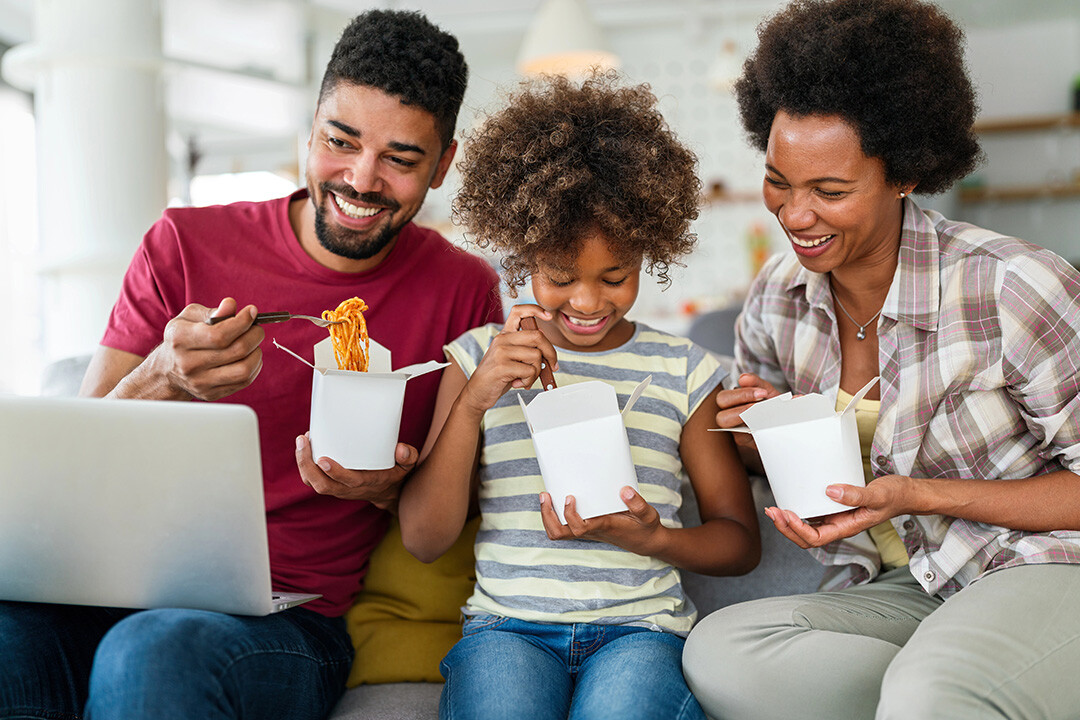 A family eats dinner while watching a streaming series on a laptop
