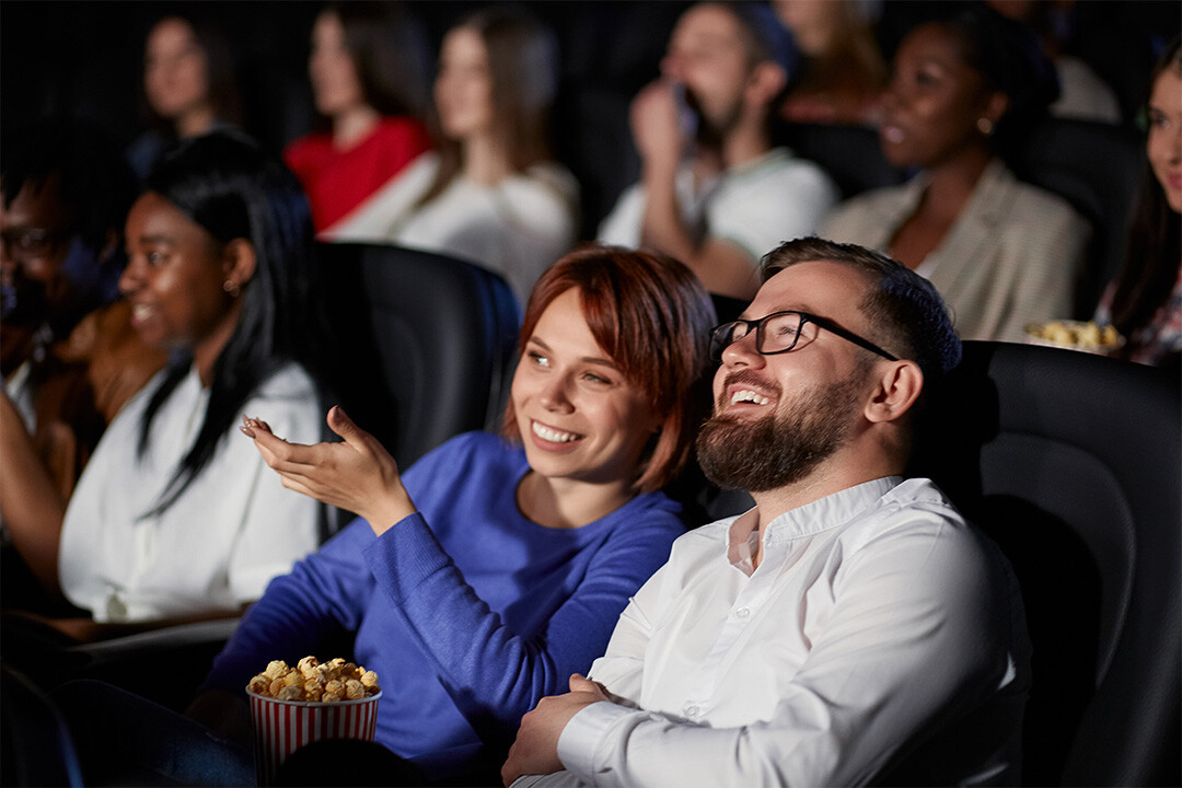 A couple sitting in a movie theater discussing the movie they are watching.