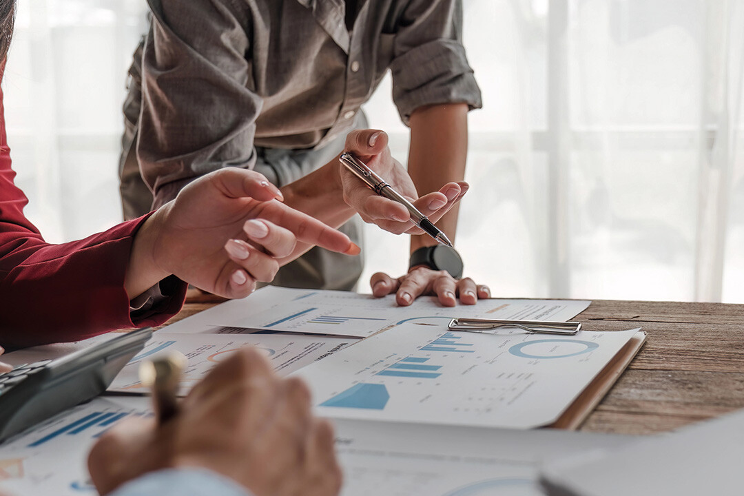 Two people work over a desk with spreadsheets and marketing numbers to ascertain data insights for their ad campaigns